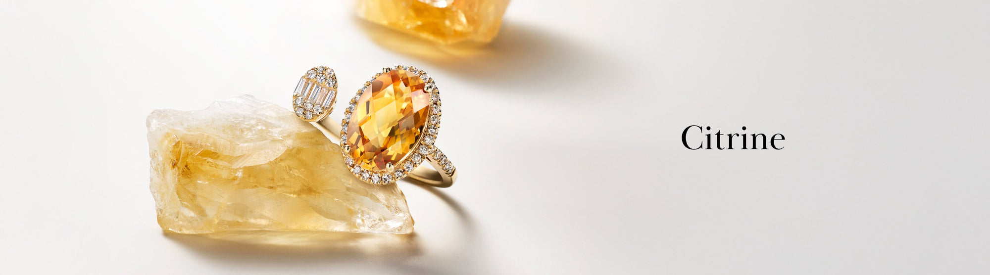 A faceted citrine gemstone ring with a diamond halo rests on a raw citrine crystal, with the word Citrine in elegant font on a clean, light background.