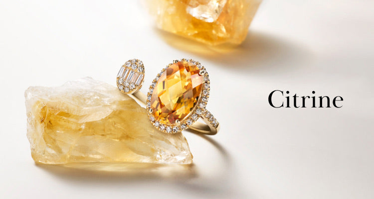 A gold ring with an oval citrine gemstone surrounded by diamonds rests on a rough citrine crystal, with the word Citrine written beside it on a white background.