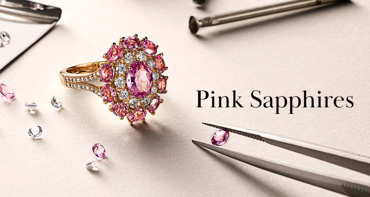 A gold ring with pink and clear gemstones is displayed on a light surface, surrounded by loose pink and clear stones, tweezers, and tools. The words Pink Sapphires appear on the right.