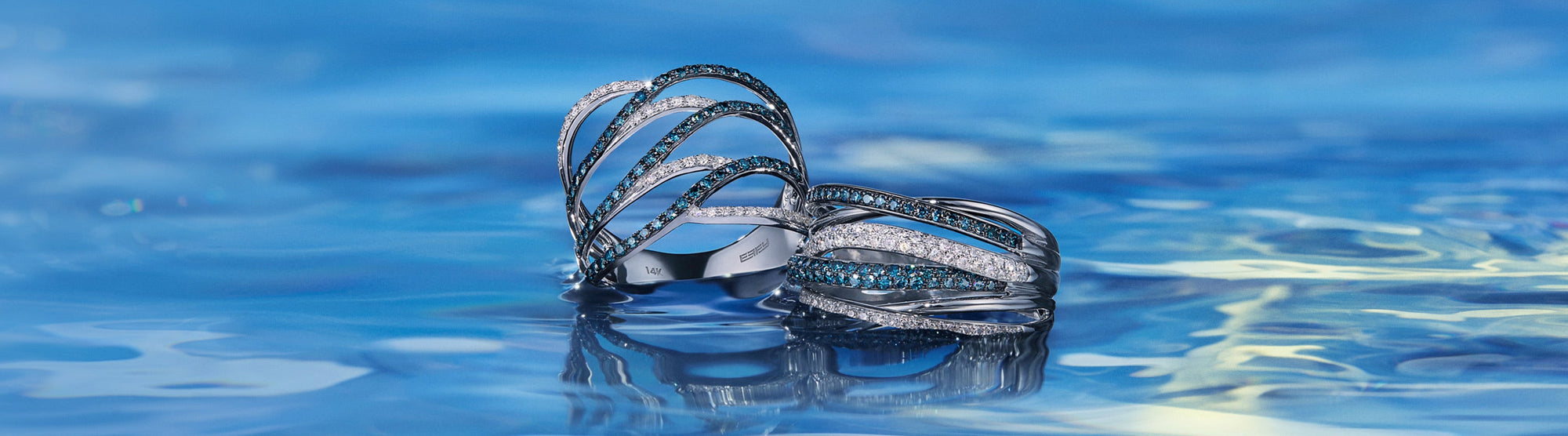 Gold necklace and ring with intertwined loops featuring blue and white diamonds are displayed on sandy textured background. Text reads Blue Diamonds.