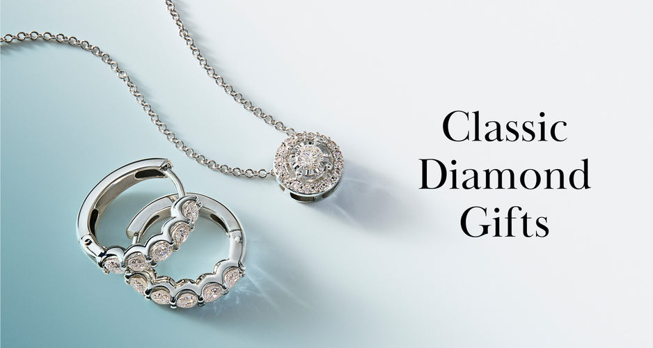 A silver necklace with a round diamond pendant and a pair of diamond hoop earrings are displayed on a light blue surface next to the text Classic Diamond Gifts.