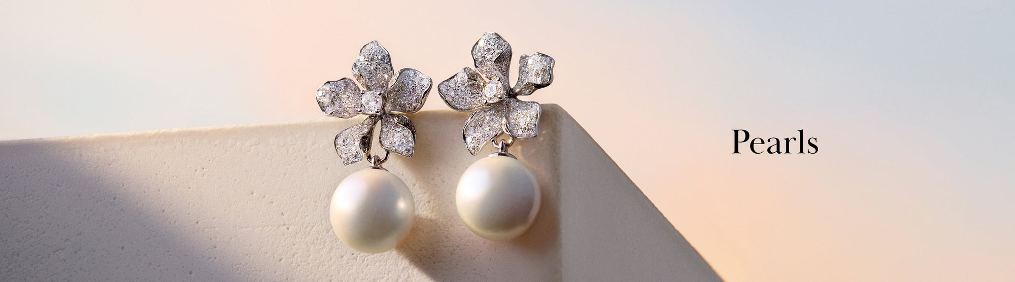Close-up of elegant pearl earrings with intricate, sparkling floral designs, displayed on a beige surface against a soft pastel background. The word Pearls appears on the right.