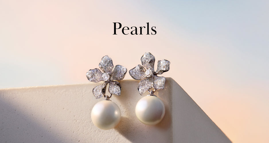 A pair of elegant earrings with sparkling floral-shaped tops and large, round pearls hanging below, displayed on a light surface with a pastel sky background. The word Pearls is written above.