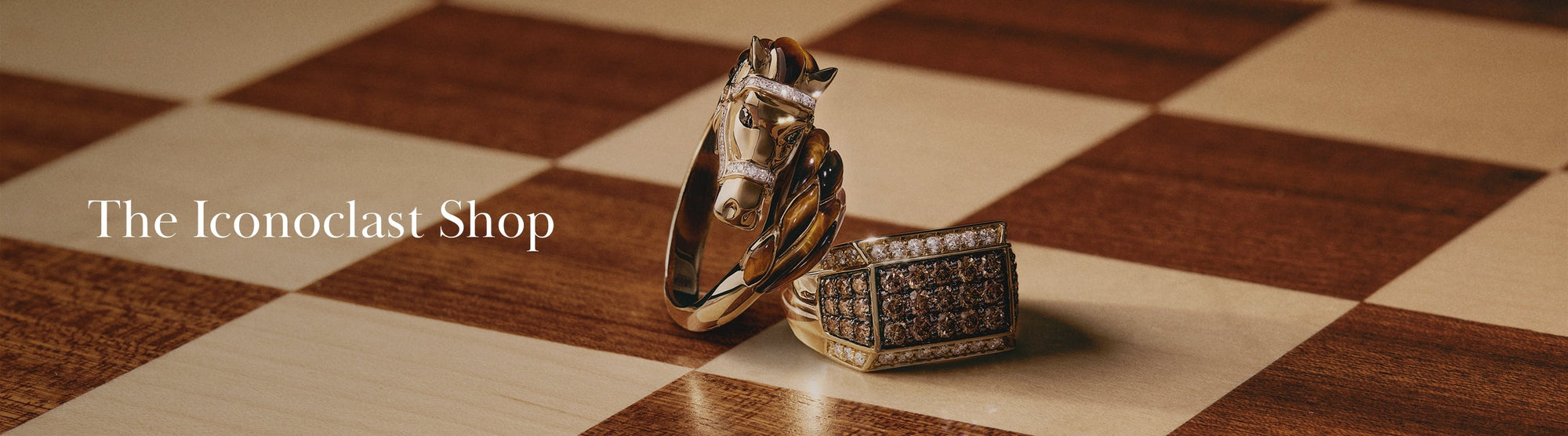 A gold horse-head bracelet and a gem-studded rectangular ring rest on a chessboard beside the text The Iconoclast Shop.