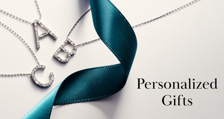 Three silver necklaces with diamond-studded letter pendants A, B, and C are displayed beside a teal satin ribbon and the words “Personalized Gifts” on a light background.