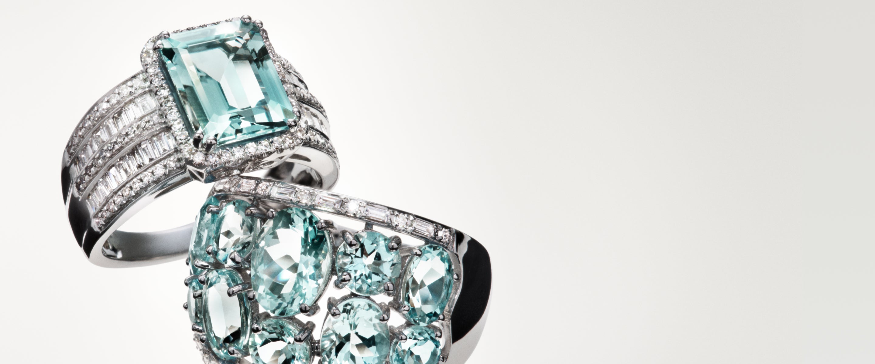 Two elegant rings with large, light blue gemstones and multiple small diamonds set in sleek silver bands, displayed against a soft, light background.