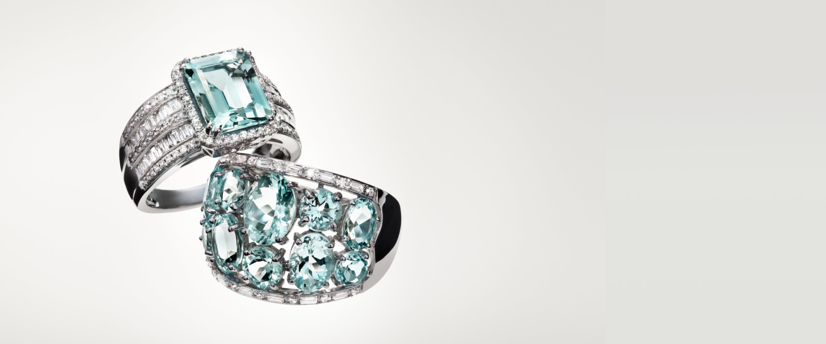 Two elegant silver rings, each adorned with light blue gemstones and surrounded by small sparkling diamonds, displayed against a plain off-white background.