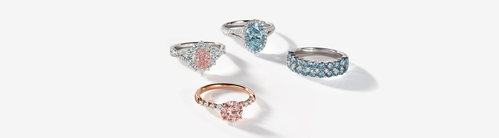 Four gemstone rings on a white background: two feature pink stones, one with a gold band, and two feature blue stones with silver bands adorned with smaller clear stones.