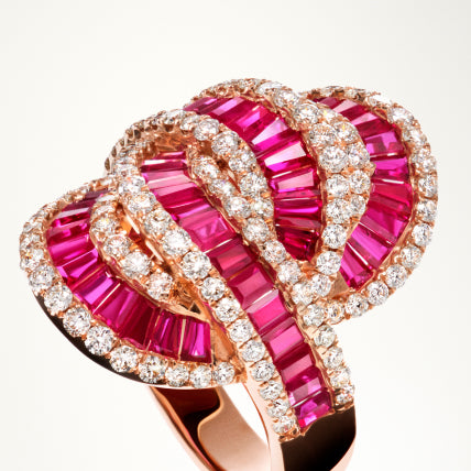 A gold ring features an intricate, looping design with rows of vibrant pink gemstones and sparkling white diamonds set in alternating patterns.