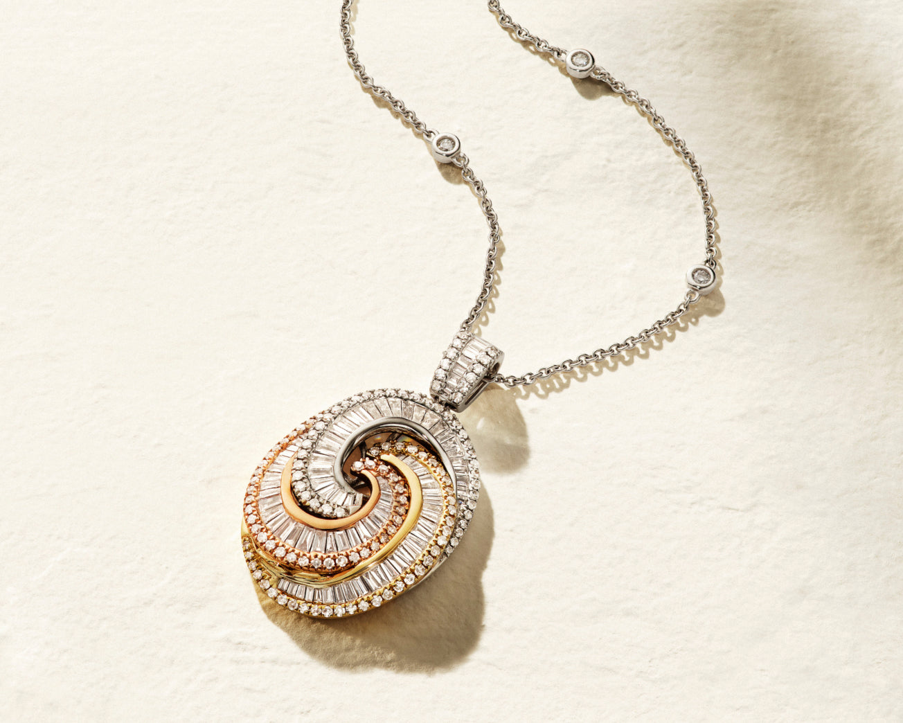 A necklace with a pendant featuring intertwined loops in yellow, rose, and white gold, adorned with small diamonds, displayed on a light textured background.