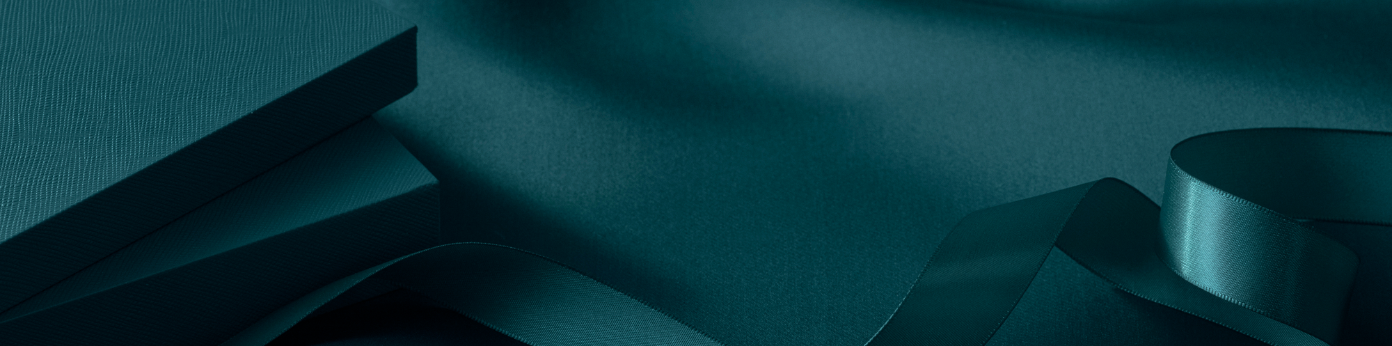Teal-colored gift boxes and satin ribbon rest on a matching teal fabric background, creating a sophisticated and elegant look.