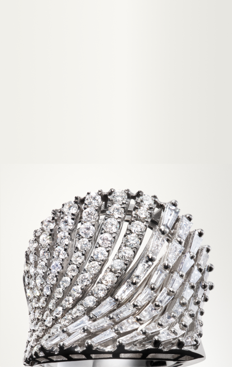 A luxurious silver ring with multiple rows of sparkling round and baguette-cut diamonds arranged in a wave-like, fan-shaped pattern against a light background.