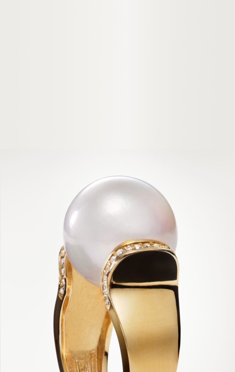 A gold ring featuring a large, round white pearl centerpiece, accented with small diamonds and black enamel detailing on the band, set against a plain white background.